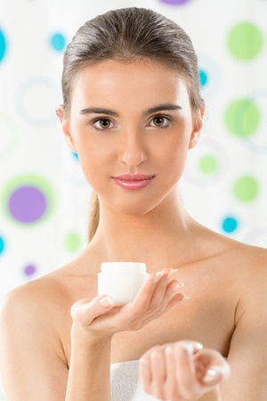 Young woman in a towel, holding a generic jar of beauty cream.