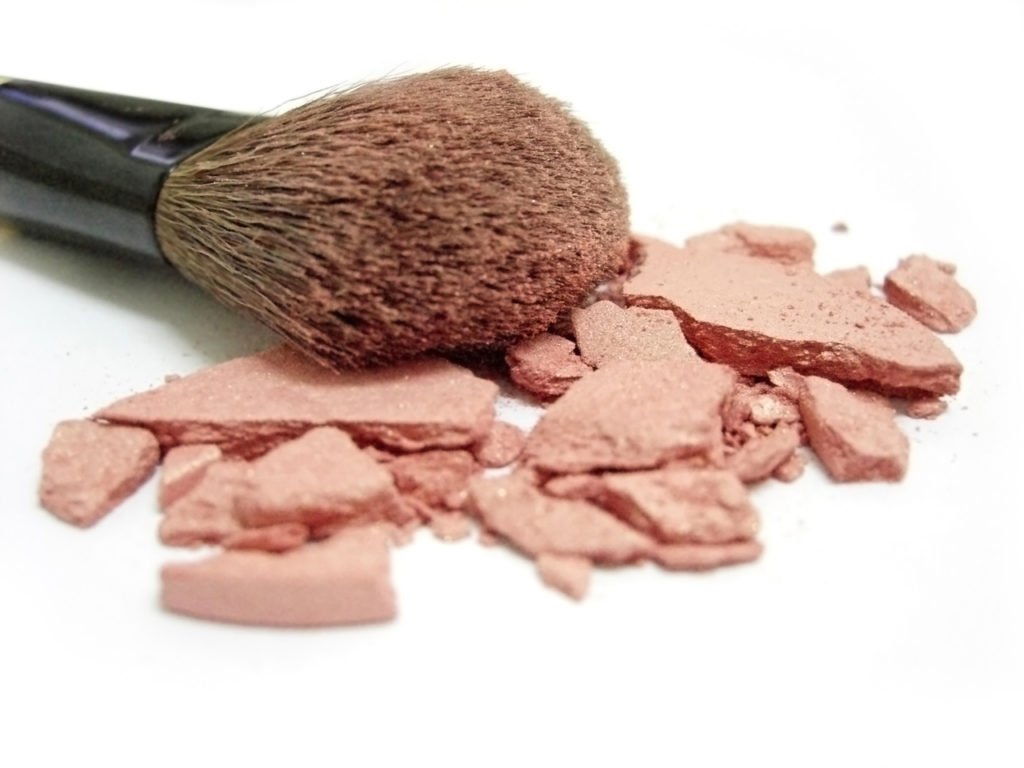 Makeup brush with crumbled eye shadow in a peachy color scattered underneath.