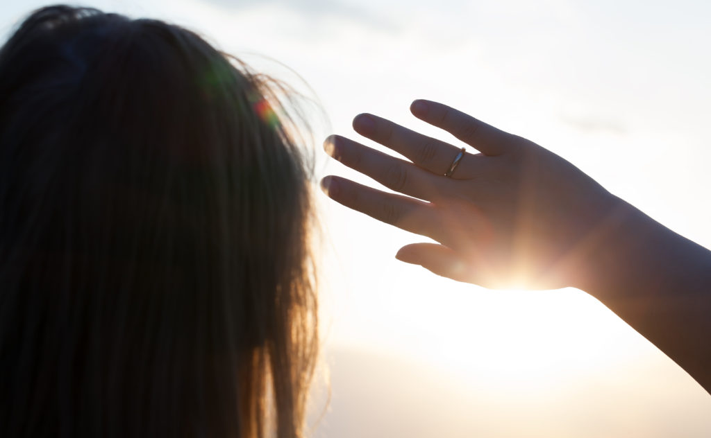 Back close-up shot of a woman looking in the distance hiding from the sun with a hand