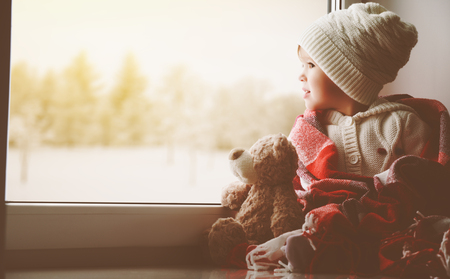 little girl sitting by the window with a teddy bear