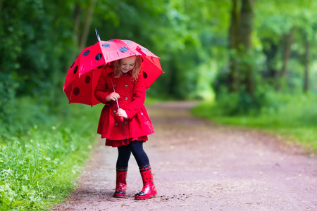 Little girl playing in rainy summer park.