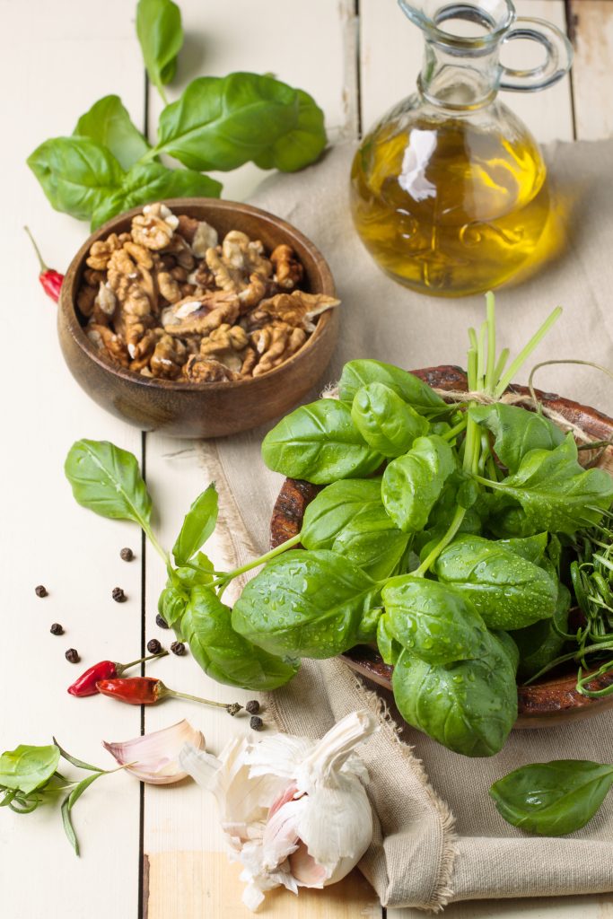 Bunch of fresh basil, bowl of walnuts, pepper, garlic and glass bottle of olive oil ready for 16 minute shrimp pasta meal