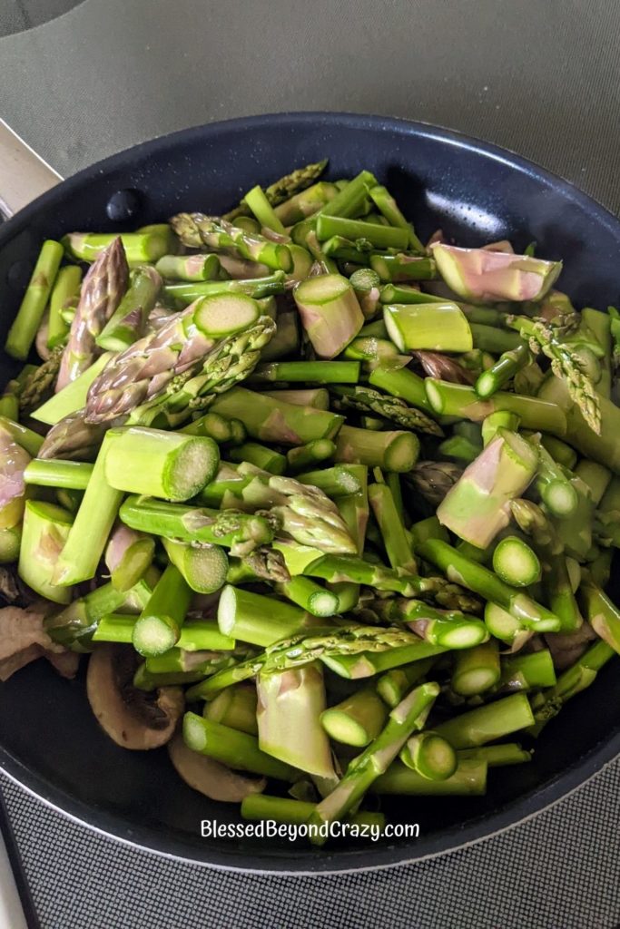 Fresh asparagus added to skillet with bacon and mushrooms