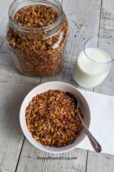 Overhead view of glass of milk, bowl of granola, and jar of granola.