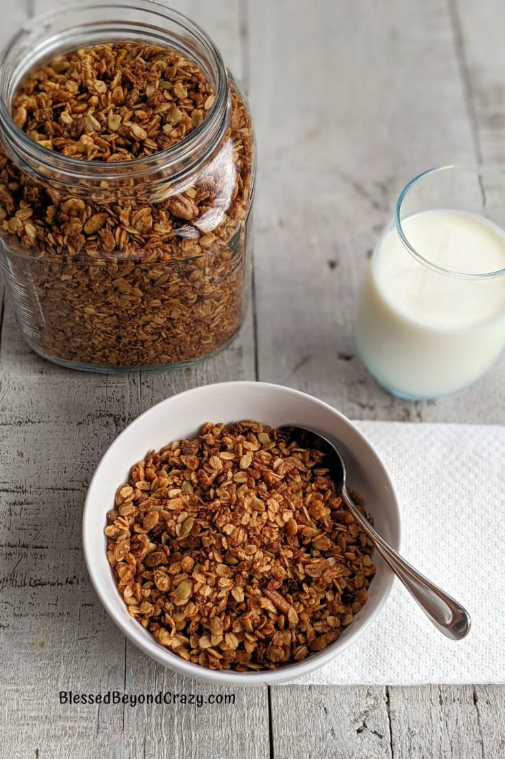Jar of granola, glass of milk, and bowl of granola ready to consume.