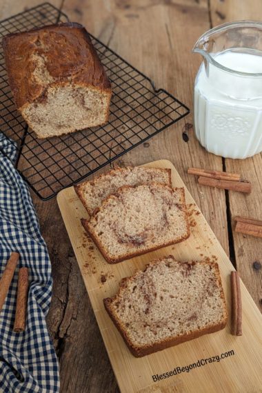 Fresh loaf of cinnamon swirl coffee cake with several servings, a pitcher of milk and several cinnamon sticks.