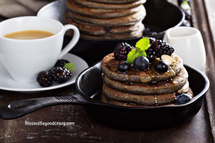 Close up of a stack of blueberry buckwheat pancakes with fruit and a cup of coffee.