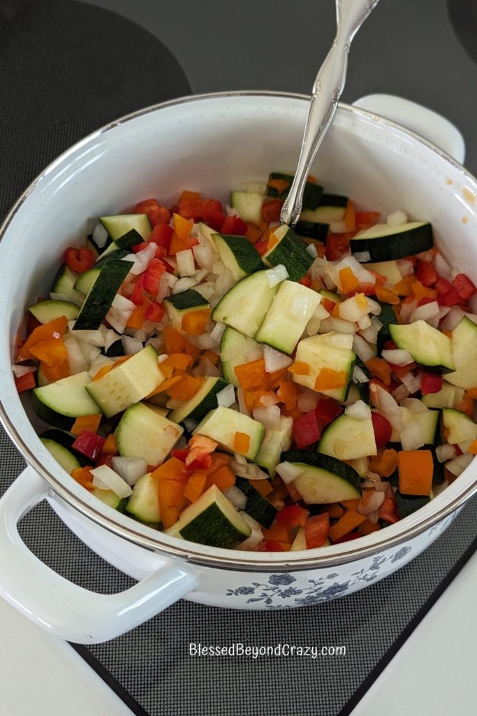Mixture of zucchini, onion, and peppers in a saucepan.