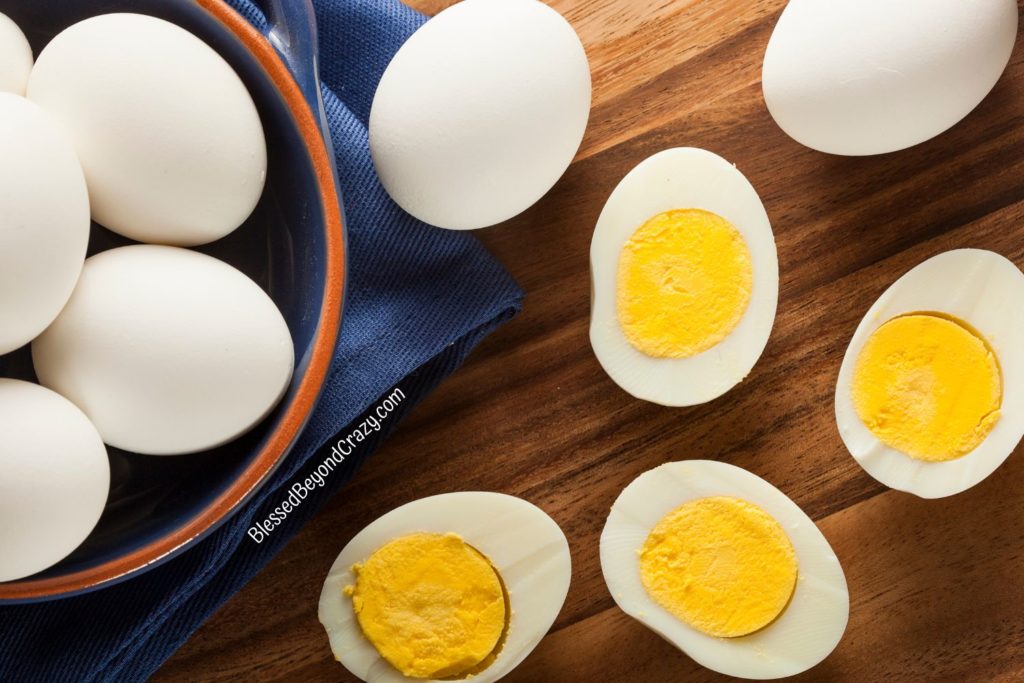 Overhead view of hard boiled eggs in a bowl and two cut eggs showing yellow yolks.
