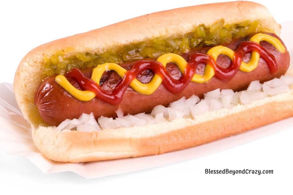 Close up of a hot dog in a bun with chopped onions, ketchup, mustard, and homemade sweet pickle relish.