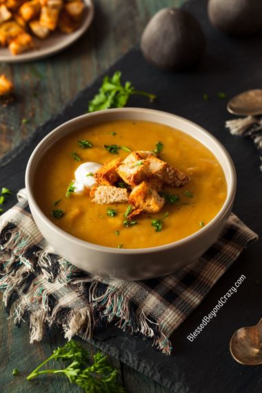 Ready to eat bowl of butternut squash soup garnished with dollop of coconut cream, fresh parsley, and crunchy croutons.