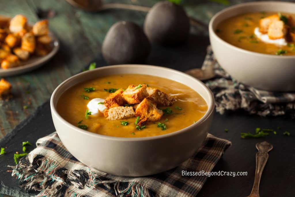 Close up view of two bowls of soup garnished with croutons, parsley and dollop of coconut cream.