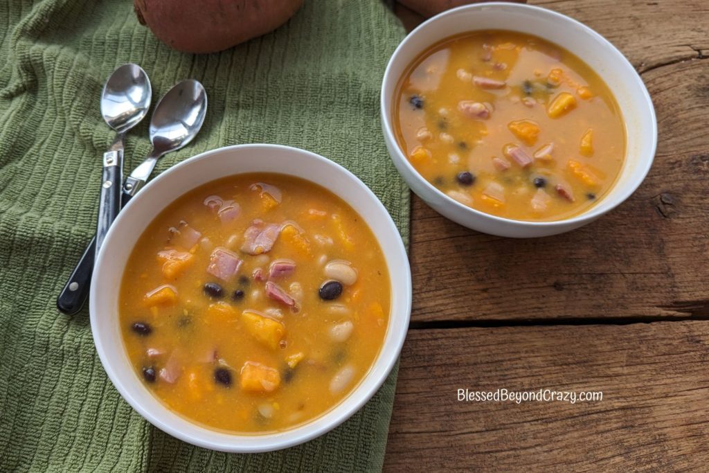 Horizontal view of two white bowls of Ham, Sweet Potato and Bean Soup.