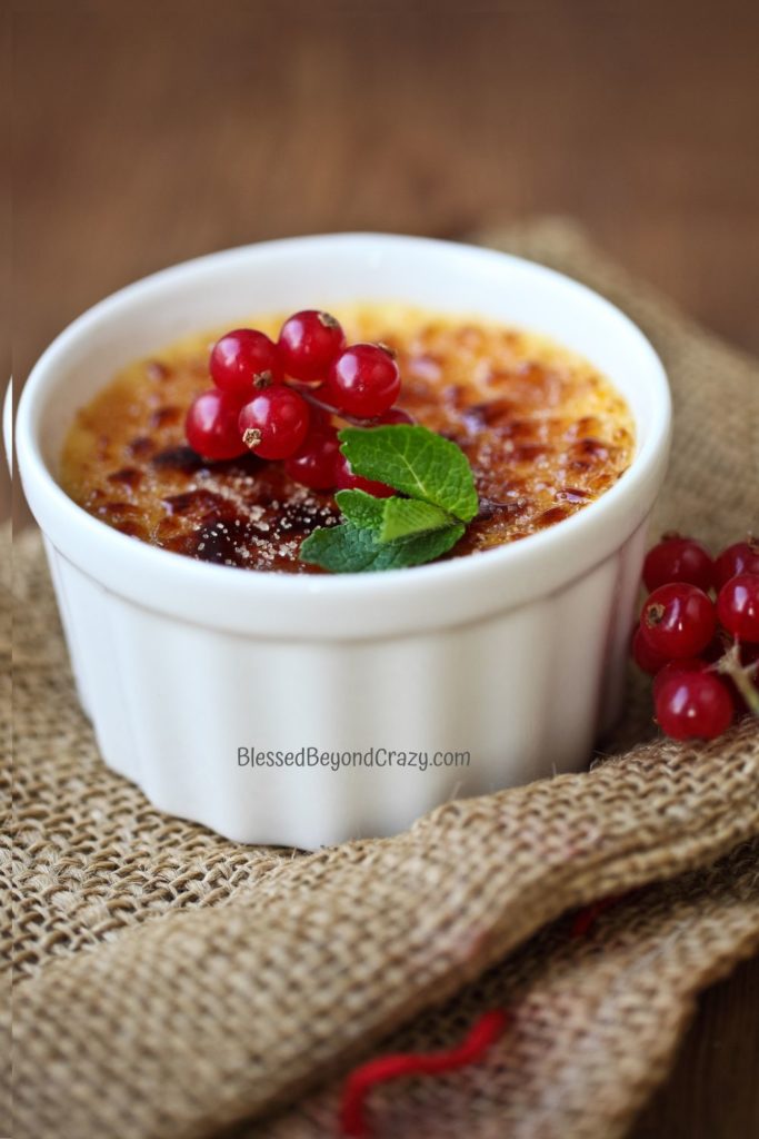 Ramekin of creme brulee topped with currants and mint leaf.