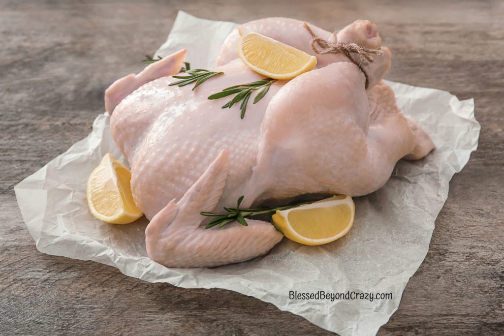 Uncooked, raw whole chicken with lemon wedges and sprigs of rosemary.