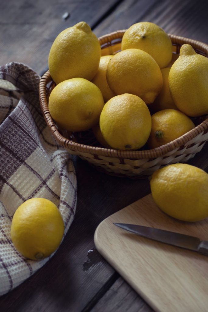 A wicker basket of whole lemons and wooden cutting board and knife.