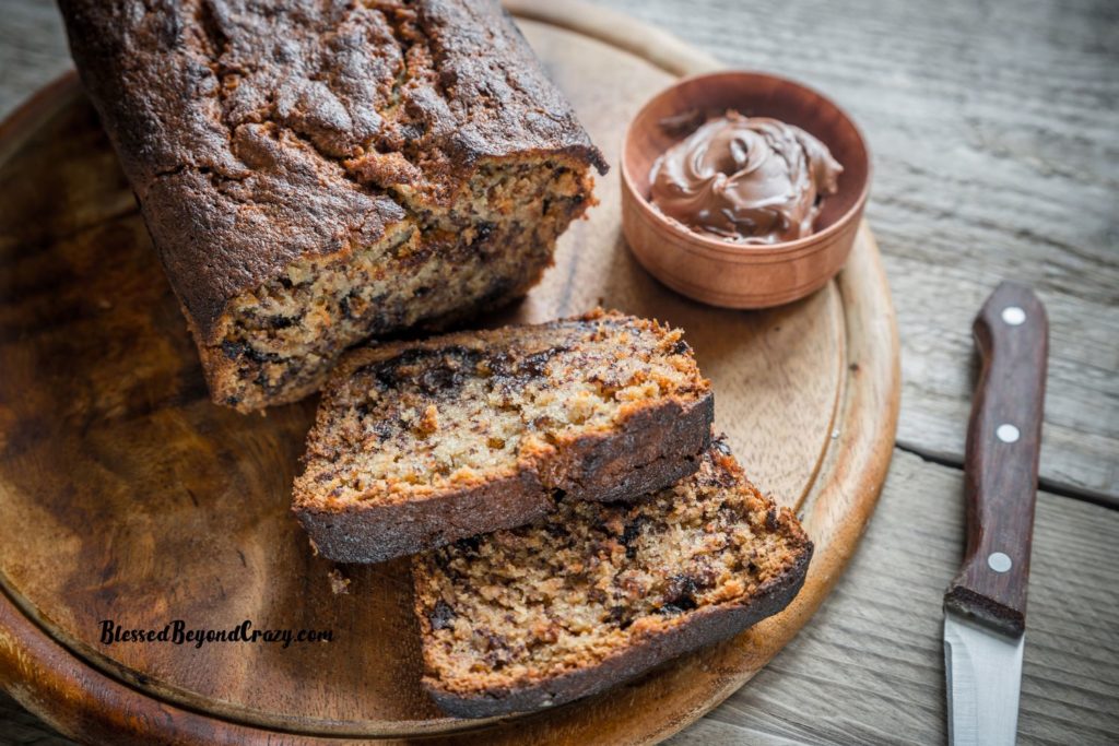 Horizontal and overhead view of loaf and two slices of Nutella Banana Bread with small bowl of Nutella off to the side.