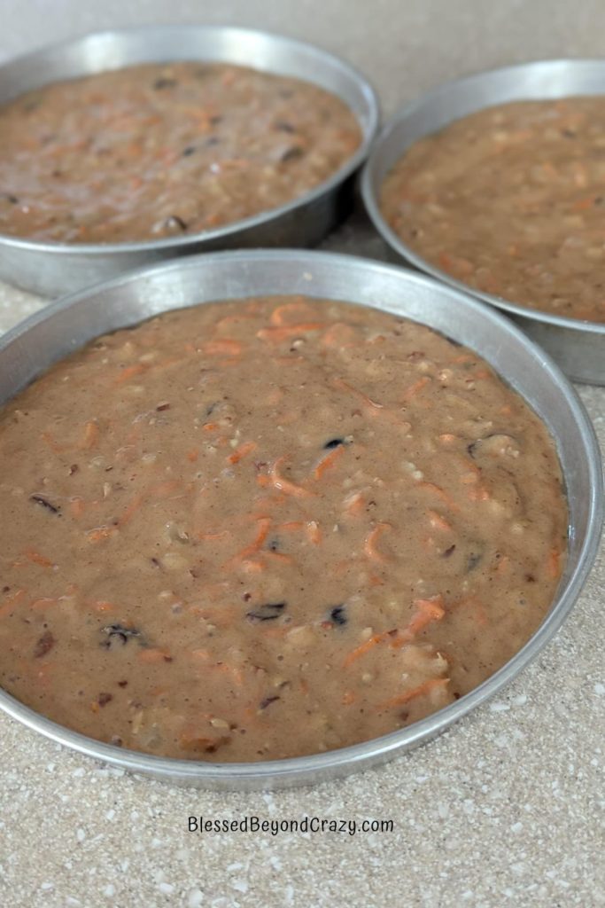 Cake cake batter divided into three baking pans ready to place into the oven.