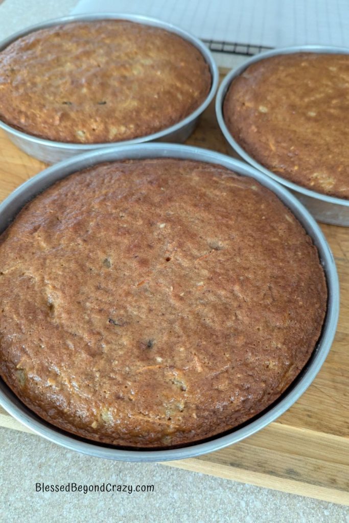 Three cake pans with freshly baked carrot cake cooling.