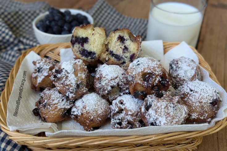 Horizontal view of basket with blueberry fritters and one fritter cut in half.