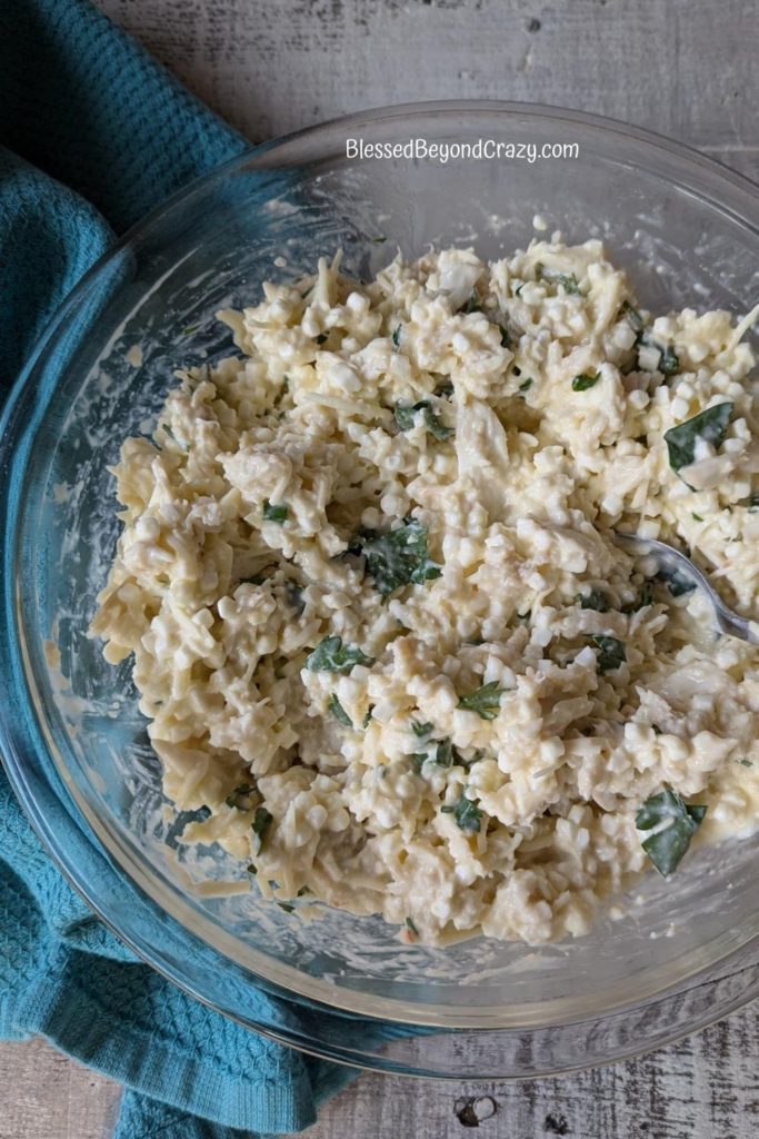 Clear glass bowl with mixture of ricotta cheese, Italian cheese blend, and parsley.