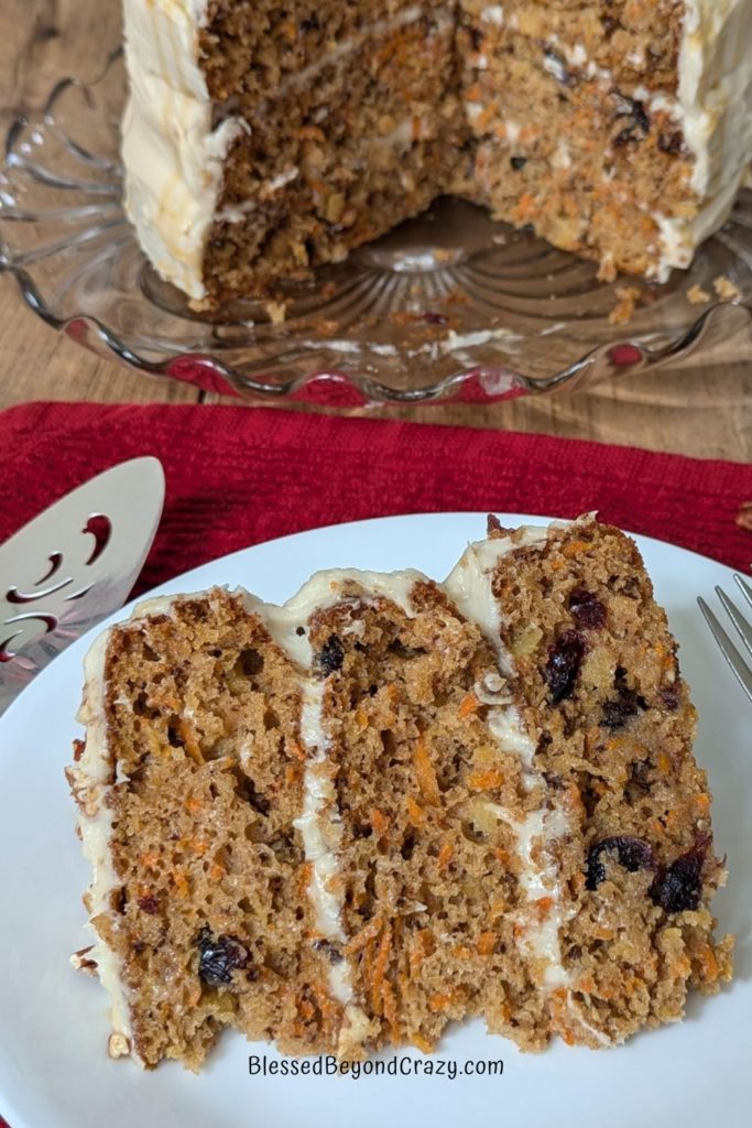 Close up view of individual serving of cranberry pineapple pecan carrot cake with remaining cake in the background.