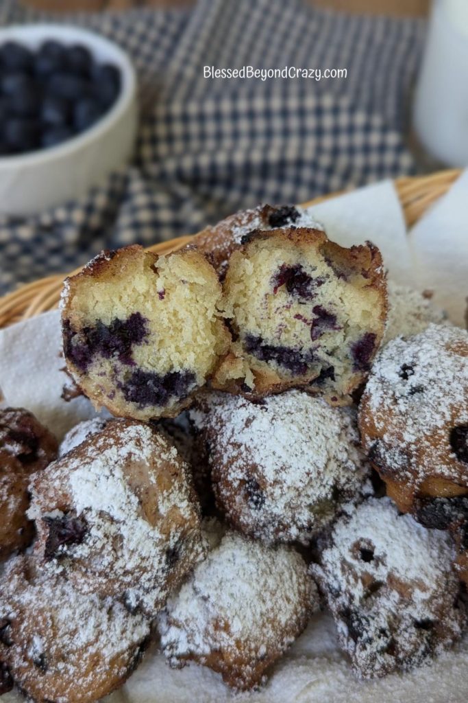 One blueberry fritter cut in half sitting on top of other blueberry fritters.