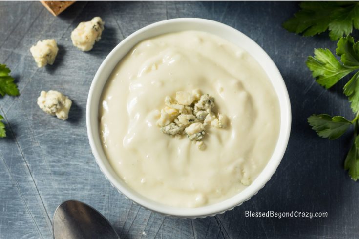 Overhead photo of a white bowl filled with blue cheese dressing, fresh parsley, blue cheese crumbles, and a spoon.