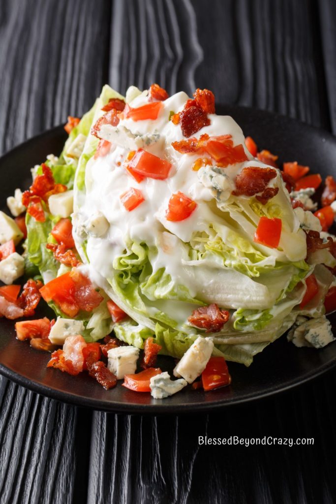 Photo of a salad wedge with chopped tomatoes, bacon crumbles, and blue cheese dressing over the top.