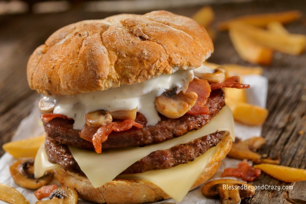 Close up photo of a two-layer hamburger with mushrooms, slices of Swiss cheese, and drizzle of blue cheese dressing.