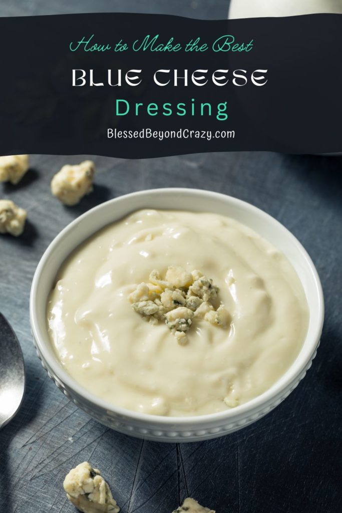 Pinterest image of a bowl of homemade blue cheese dressing and blue cheese crumbles on the table.