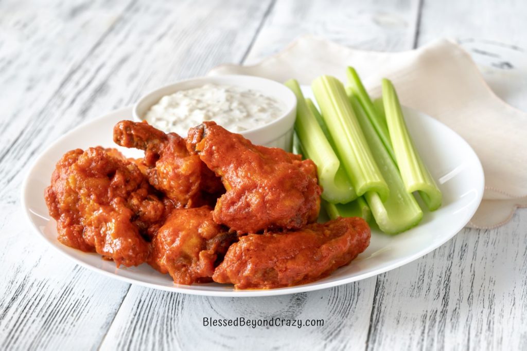 A white plate with chicken wings, celery sticks, and small bowl of homemade blue cheese dressing.