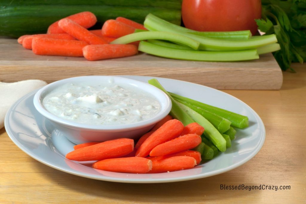 White plate with carrot and celery sticks and a smaller bowl of homemade blue cheese dressing.