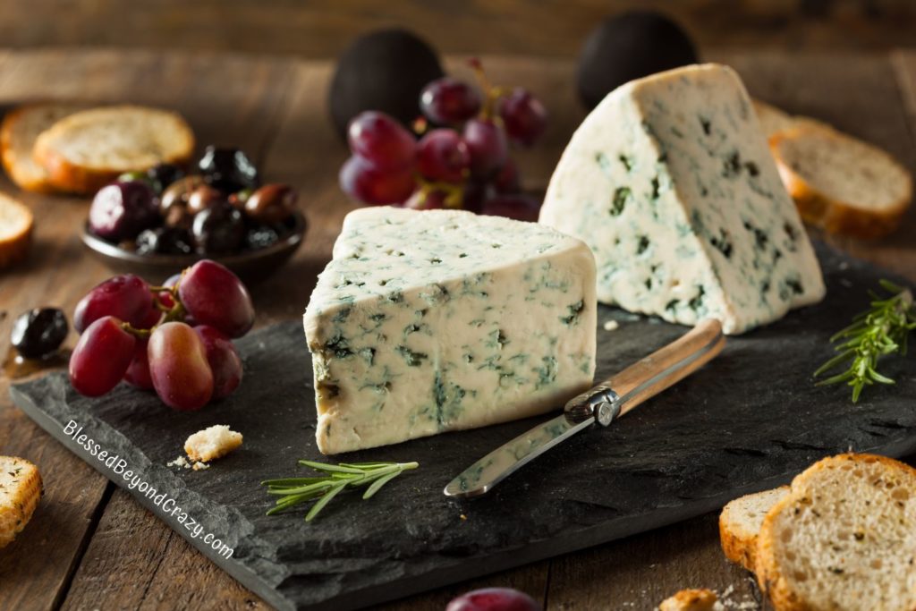 Photo of two bricks of fresh blue cheese with a small knife, grapes, and toast.