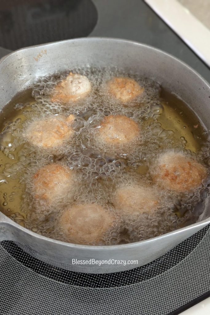 Potato Drop Doughnuts frying in hot oil on stovetop.