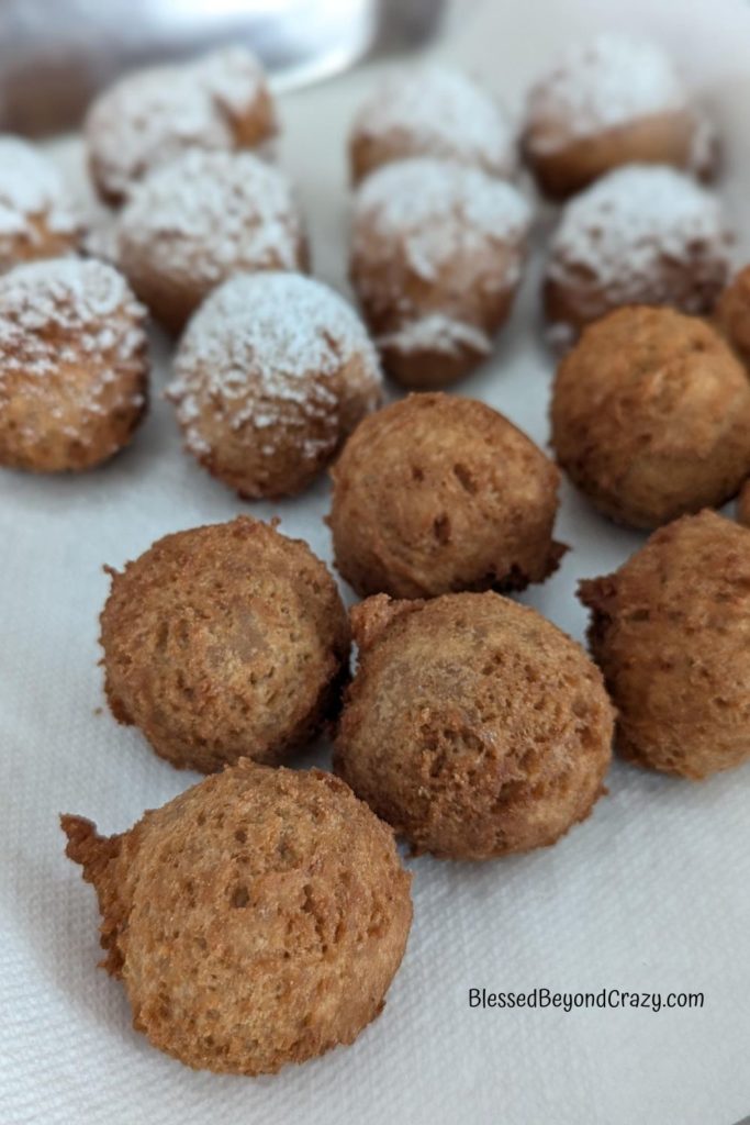 Fully cooked doughnut balls cooling on paper towels. Some doughnuts have a light dusting of powdered sugar on them.