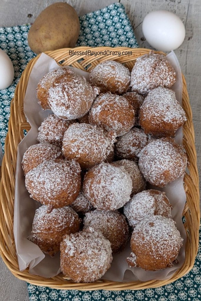 Overhead view of basket of freshly fried potato doughnuts with fresh eggs and whole potatoes in background.