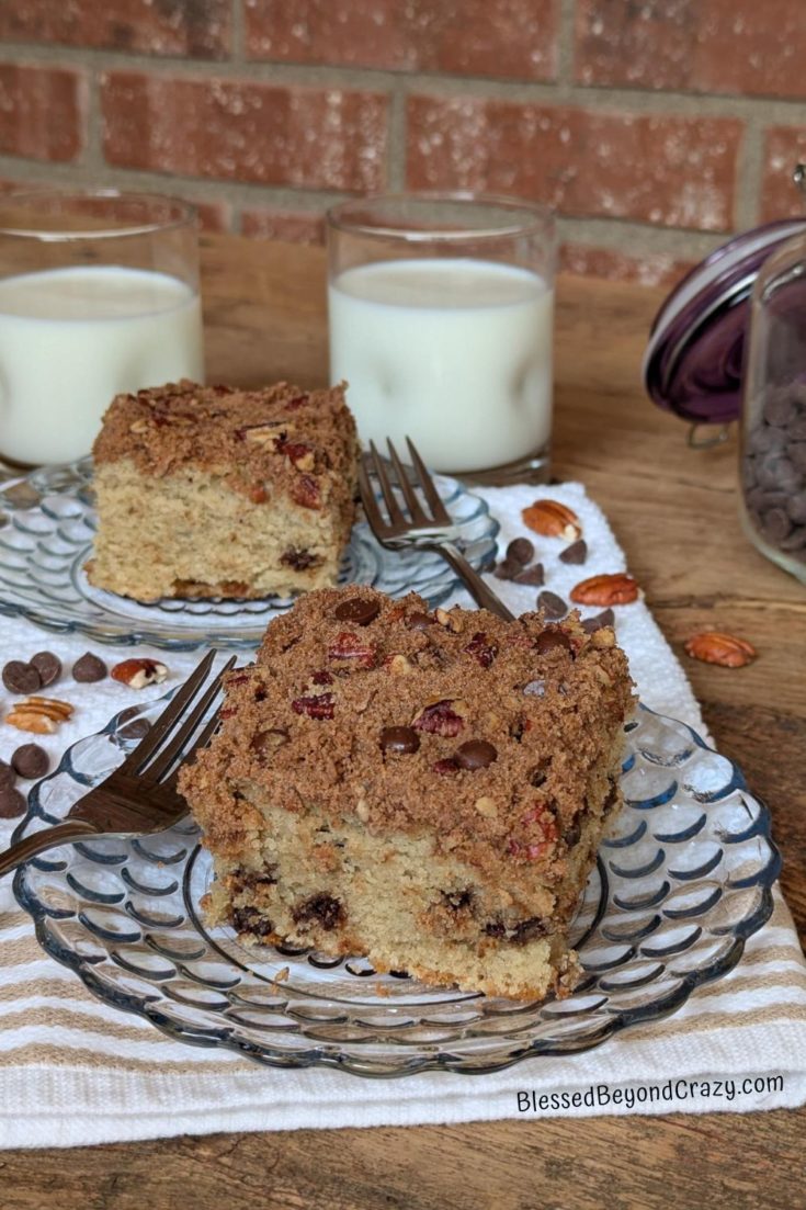 Two individual servings of chocolate chip coffee cake on glass serving plates, along with two glasses of milk.