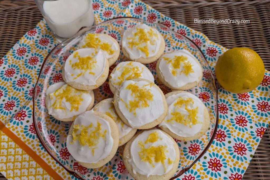 Horizontal photo of pretty glass plate with lemon cookies, glass of milk, and fresh lemon.