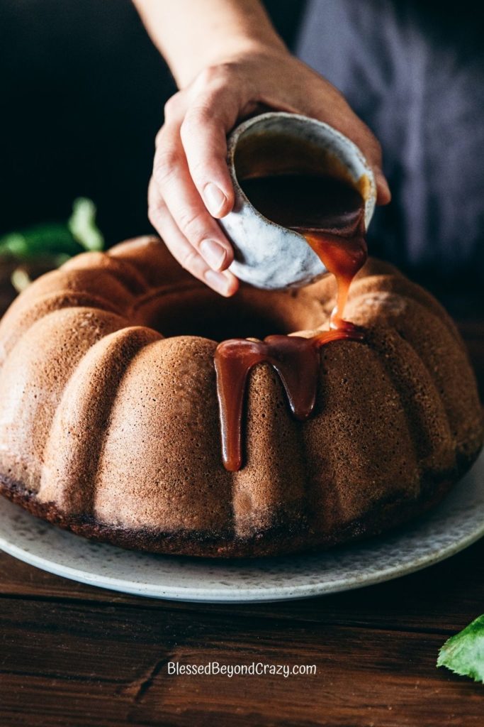 Photo of a person pouring homemade caramel sauce over an apple cider spice bundt cake.