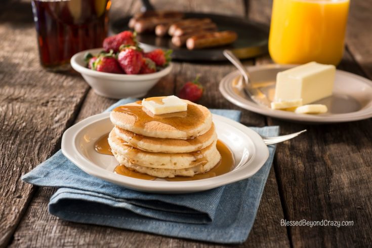 Stack of three buttermilk pancakes on a white plate with pad of butter any maple syrup on top.