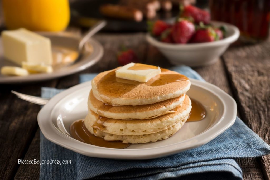 Close up horizontal photo of plate with stacked pancakes, maple syrup and butter.