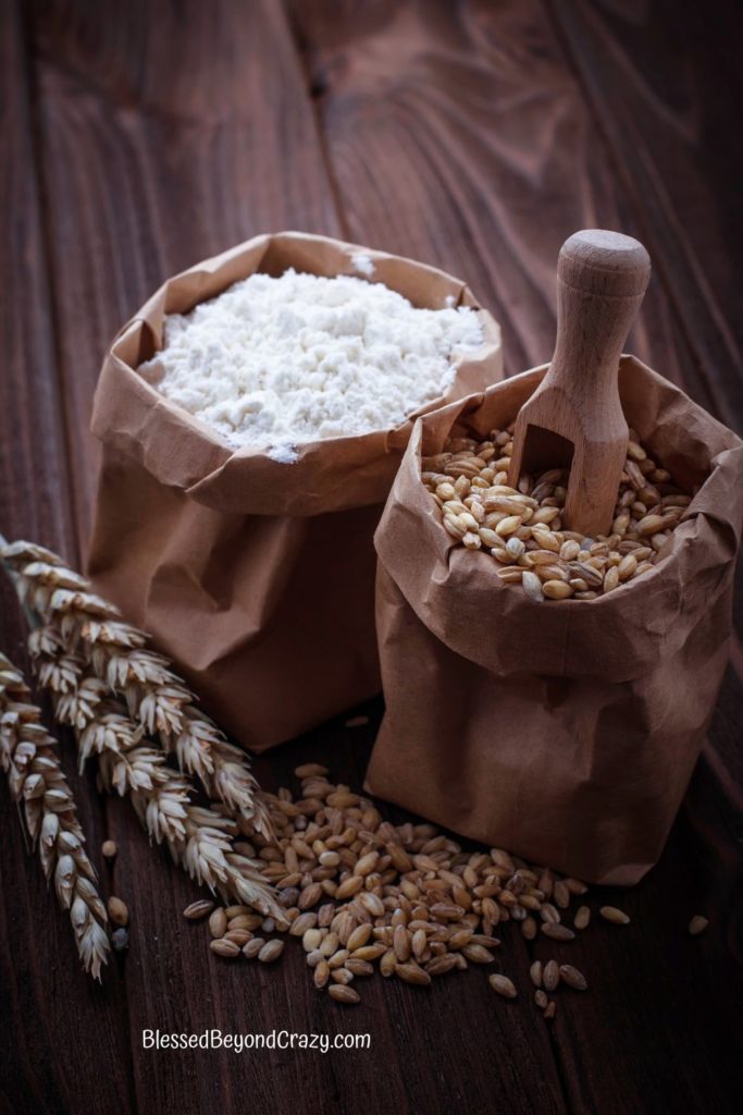 Photo of a paper bag with whole grain wheat and another paper bag with wheat flour.