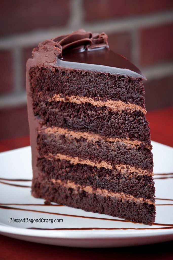 Vertical photo of a slice of 5-layered chocolate cake with chocolate icing.