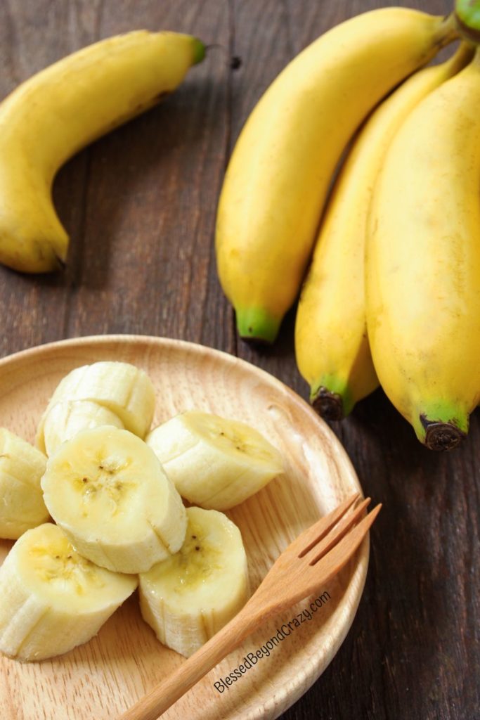 Overhead photo of ripe bananas and a wooden plate with a sliced banana and wooden fork.