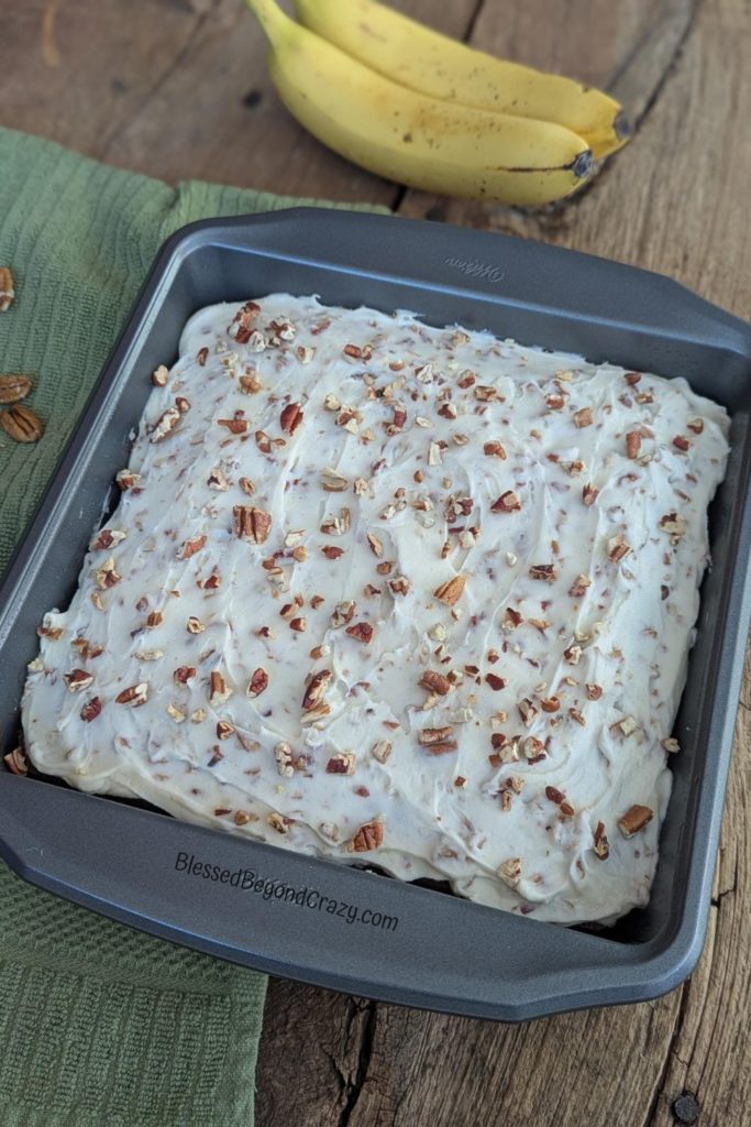 Overhead view of frosted banana pecan cake with two bananas and pecans.