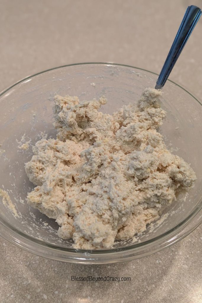 Clear glass mixing bowl with biscuit dough and spoon.