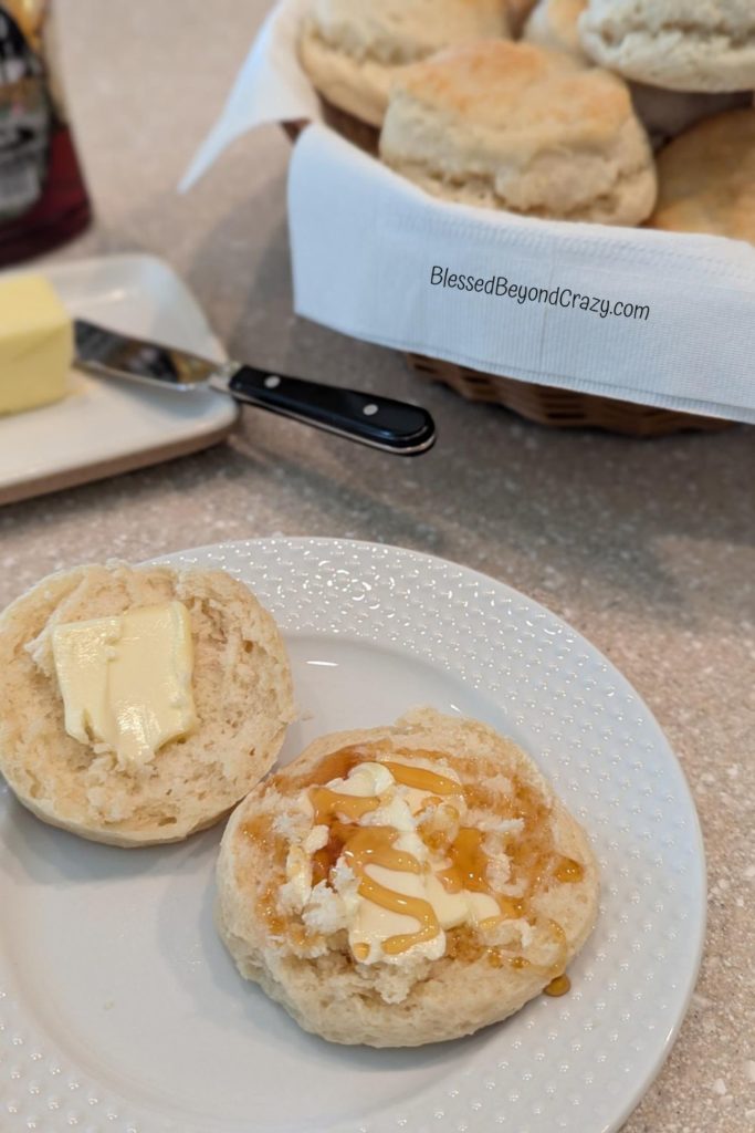 Photo of biscuit with butter and drizzle of honey as well as a basket of biscuits.