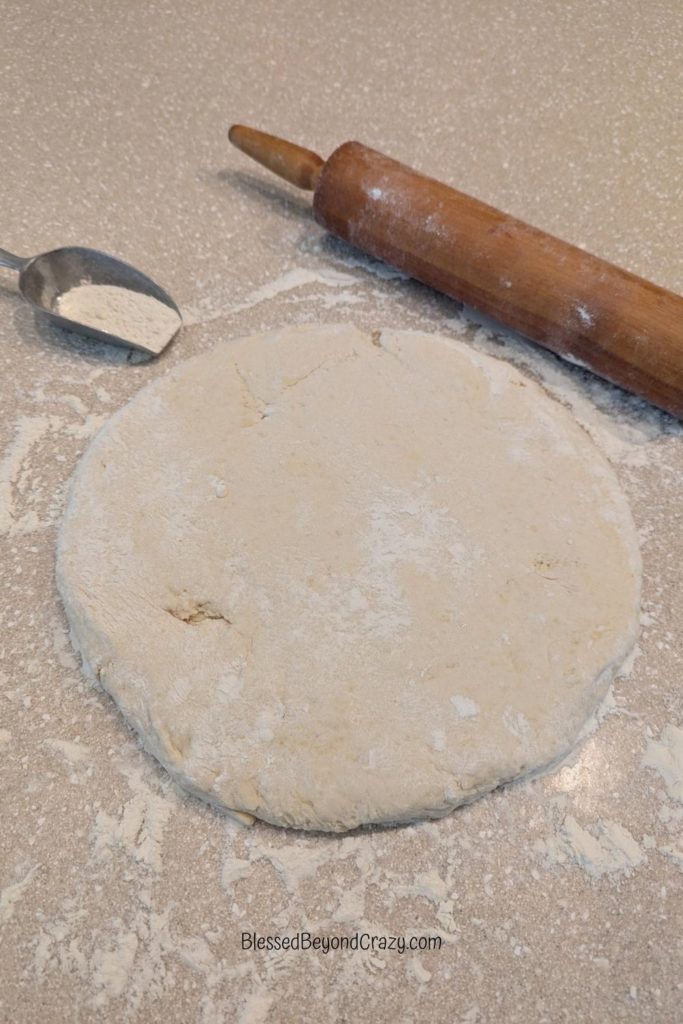 Rolled out biscuit dough with flour and wooden rolling pin.