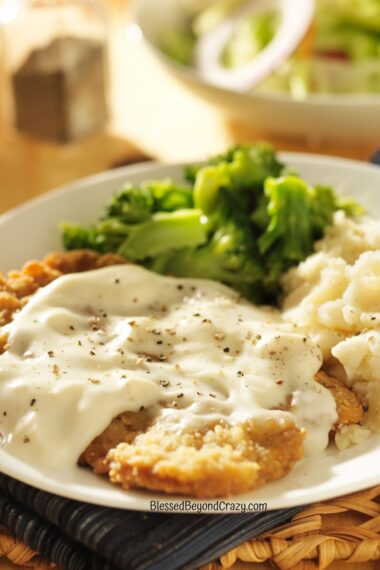 Vertical photo of white plate with chicken fried steak and gravy, mashed potatoes, and broccoli.